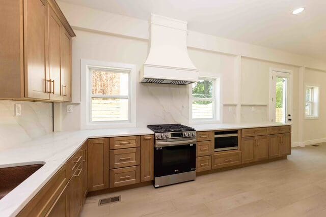 A spacious, modern kitchen with light brown cabinets, white countertops, and a stainless steel stove.